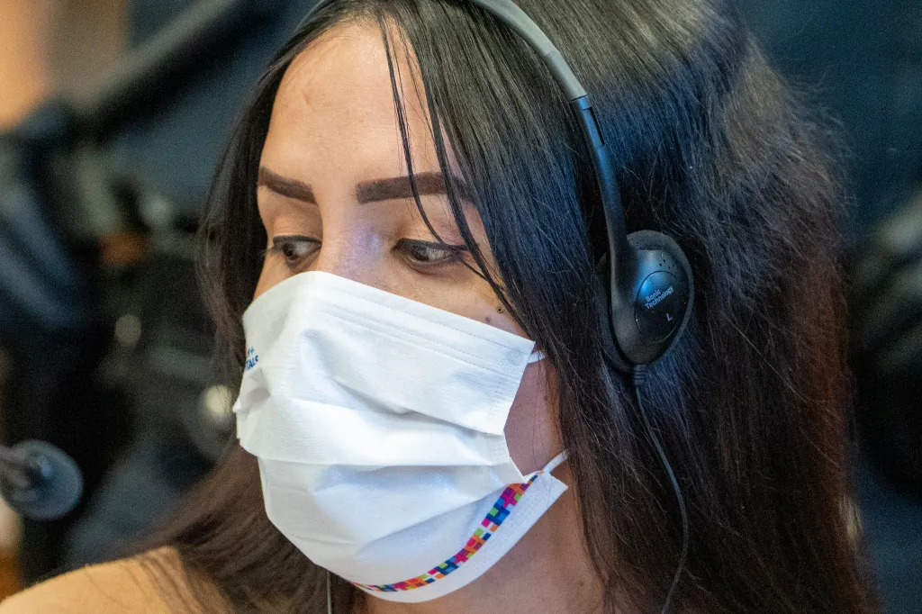 Η Nicol Suarez, μια μετανάστρια τρανς γυναίκα, φορά μάσκα και ακουστικά.